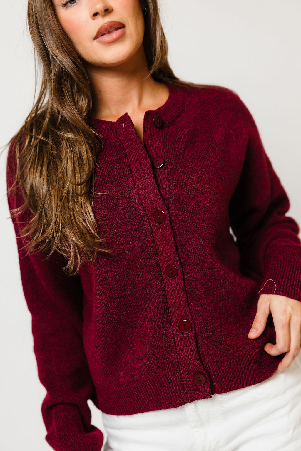 Model in the Alyssa button-front knit cardigan in deep burgundy with long sleeves, worn with white pants
