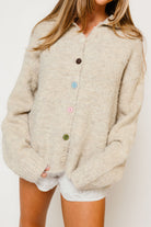 Model in the Keira funnel neck knit cardigan in a light oatmeal beige with large buttons, worn with white shorts