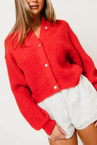 Model in the Mila chunky knit cardigan in bright red with balloon sleeves and a button front, worn with white shorts