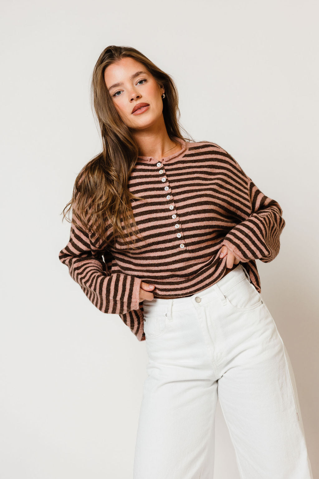 Model in the Ever oversized henley sweater with pink and dark brown horizontal stripes, worn with white wide-leg pants