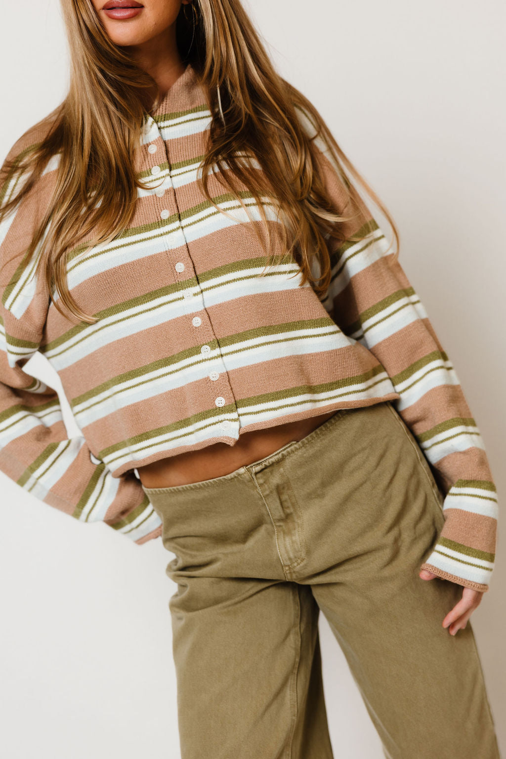 Model in the Rosemary funnel neck cardigan with tan, cream and white stripes, worn with olive wide leg pants