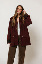 Model in the Montana barn coat in deep maroon with a collar and front pockets, worn over a white top and brown pants